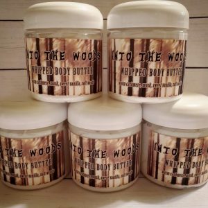 Stack of 5 jars of whipped body butter. The label shows a sketch style forest in sepia and the lettering is made to look like trees. It says "Into The Woods Whipped Body Butter" in brown text.