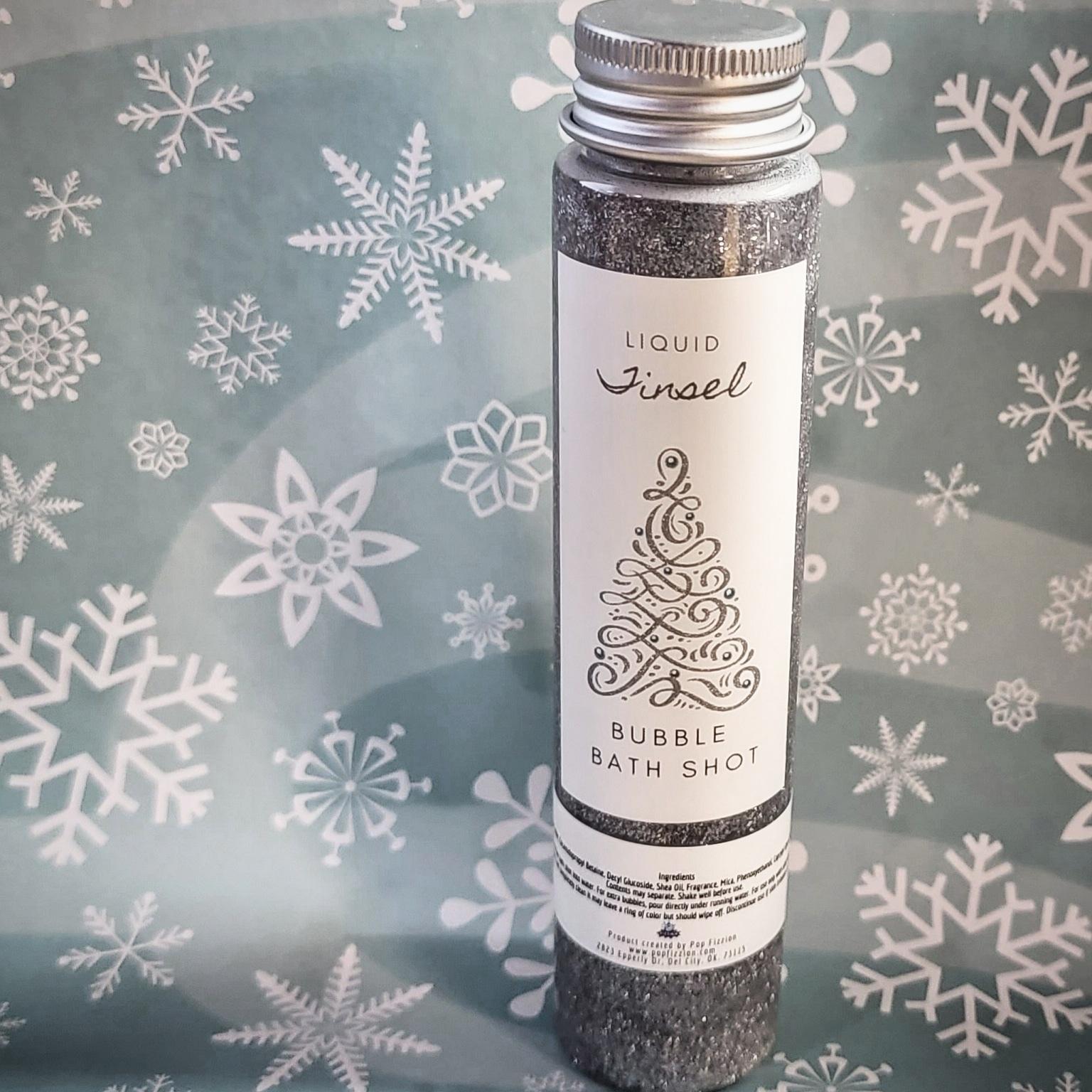 Test tube full of a very sparkly silver liquid. A label is on it with a fancy silver tree that says "Liquid Tinsel Bubble Bath Shot"